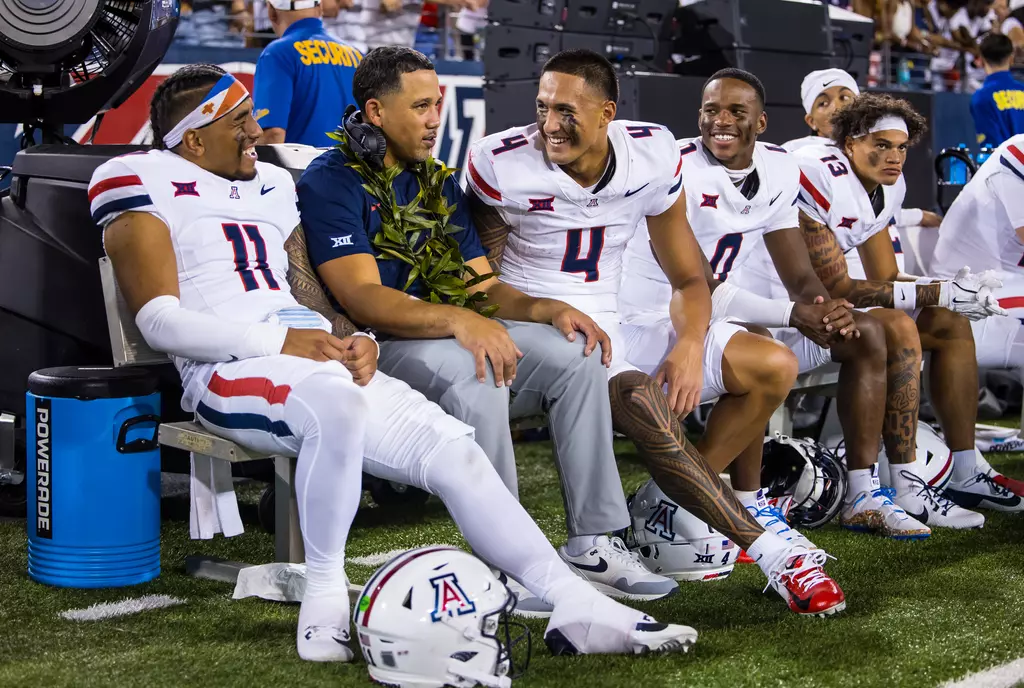 Arizona WR Tetairoa McMillan smiling on the sidelines with QB Noah Fifita, WR coach Bobby Wade, and WR Reymello Murphy.